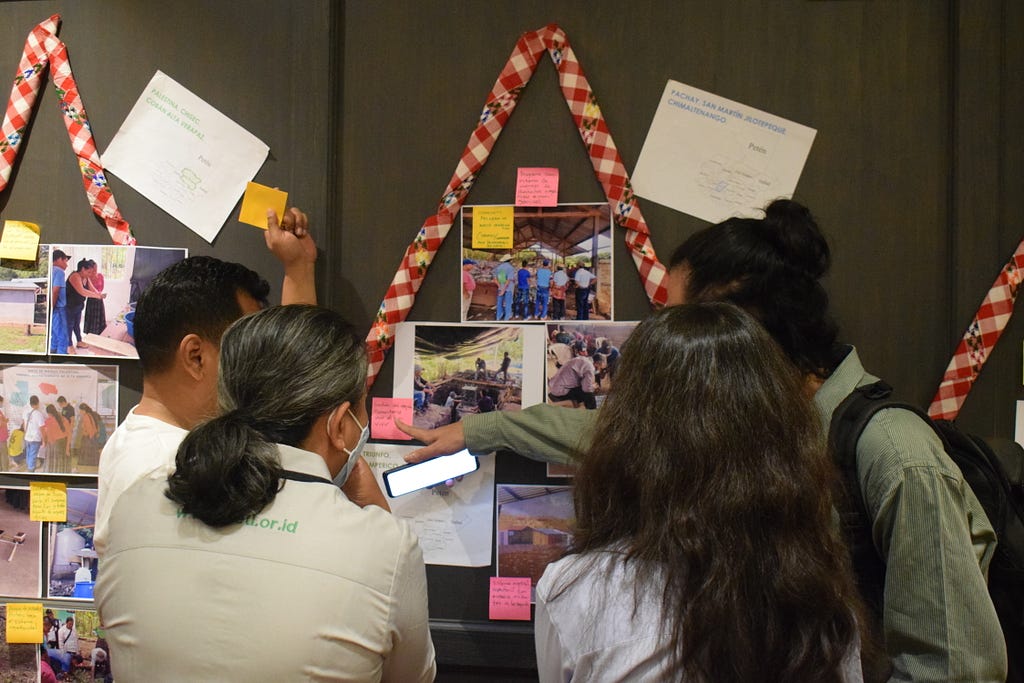 A group of four people at a workshop, discussing photos and post-it notes which are stuck on a wall.