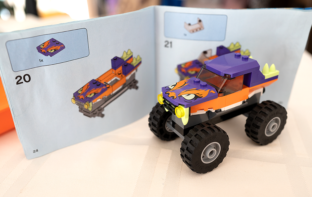 A completed Lego set of a monster truck that is roughly the size of an apple. You can see the instruction booklet in the background that illustrates one step of the build process.
