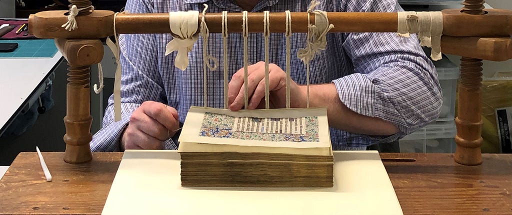 A conservator re-sewing an illuminated Latin manuscript on a traditional sewing frame