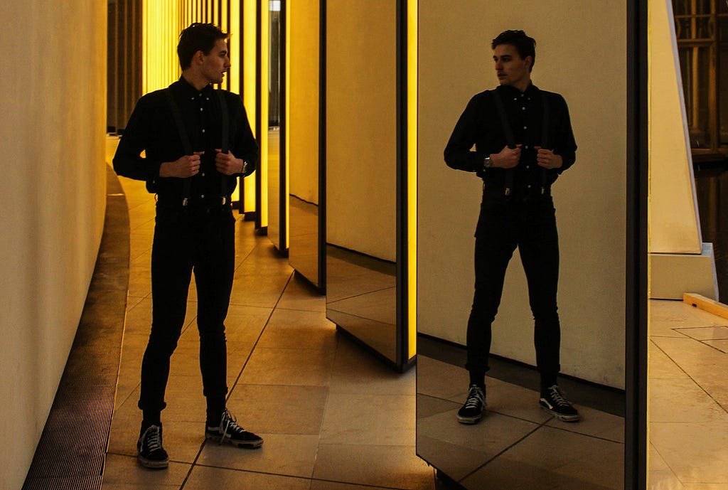 Man in expensive outfit looking at himself in a full length mirror.