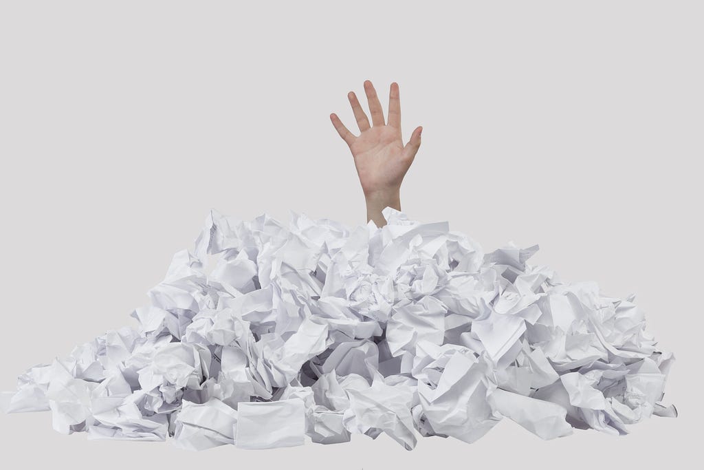 A hand emerging from a pile of scrunched up papers, looking for help