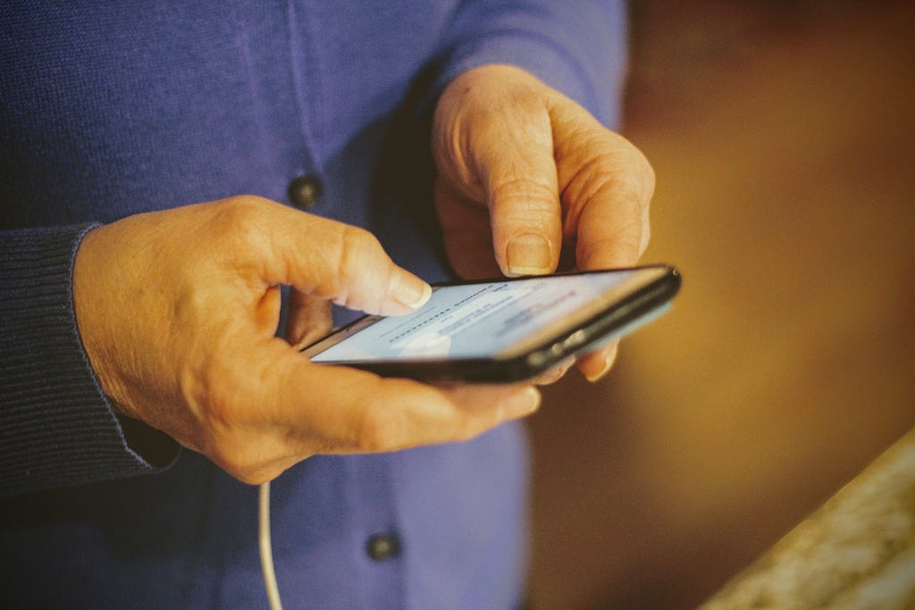 A pair of hands holding a cell phone in their hand and typing.