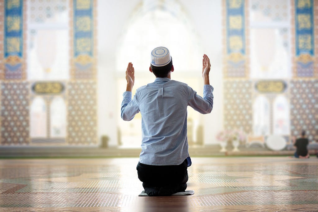 A kneeling man praying within a light, open space in a mosque.