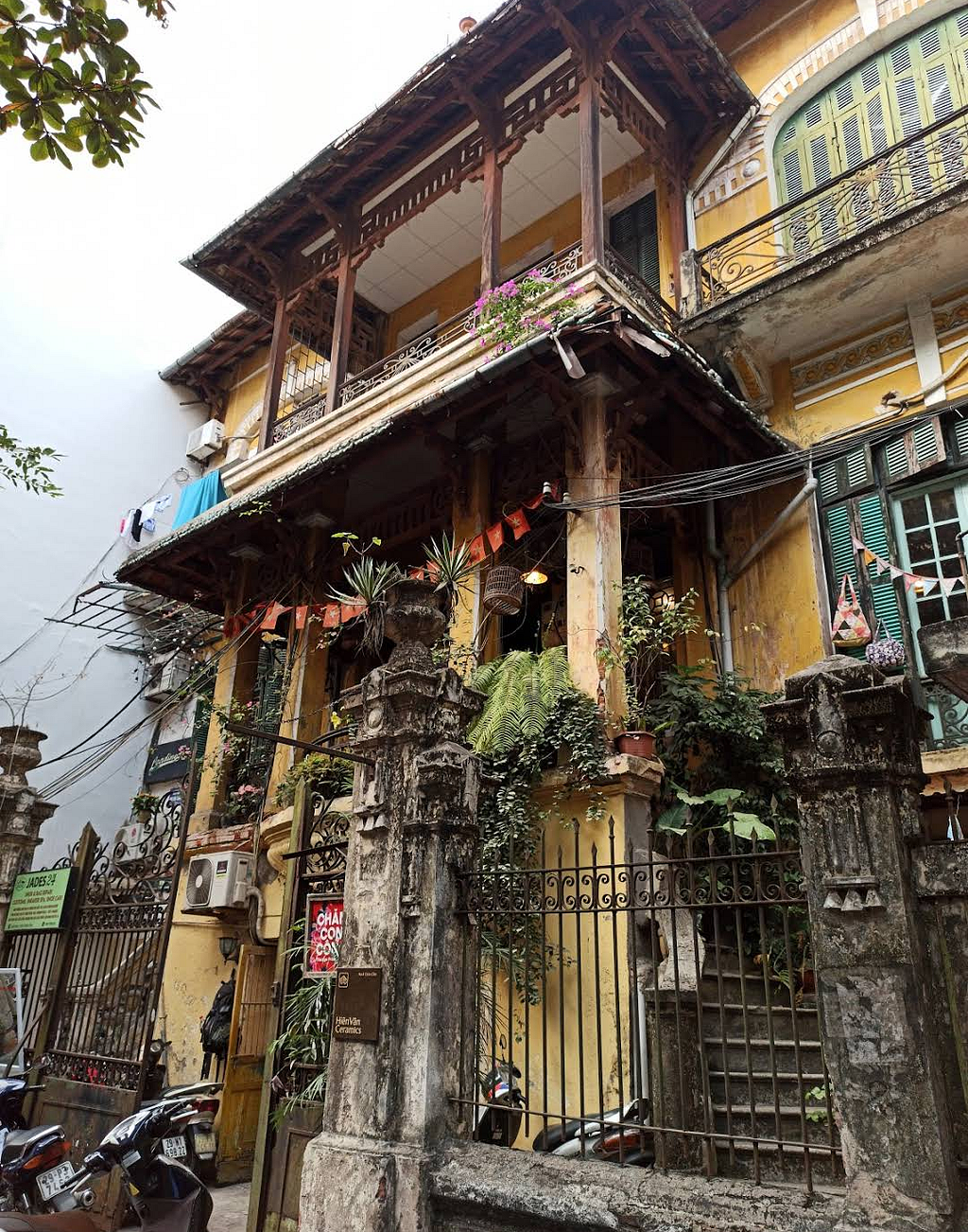 Old yellow building with large front porch and overgrown plants on stone steps in Hanoi