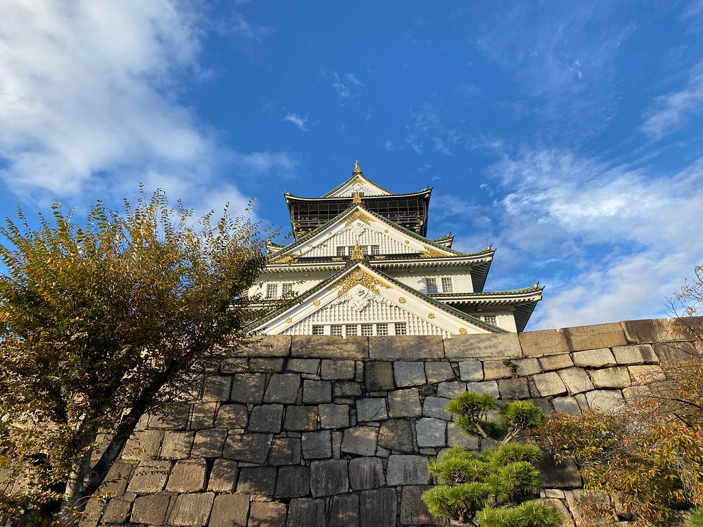 a view of the royal palace of Osaka on a sunny dat next to colorful trees