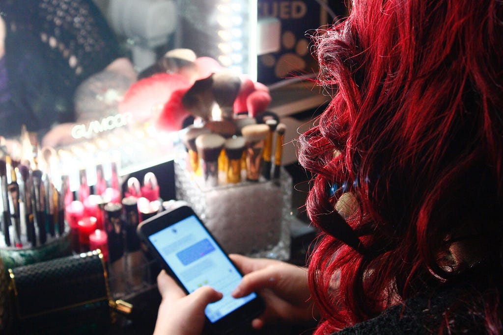 Woman sitting at her makeup counter seen from over her shoulder texting on an iPhone.