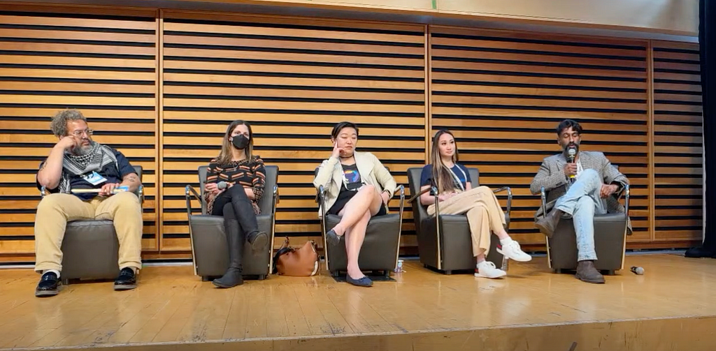 Five panelists (2 men and 3 women) at a conference panel