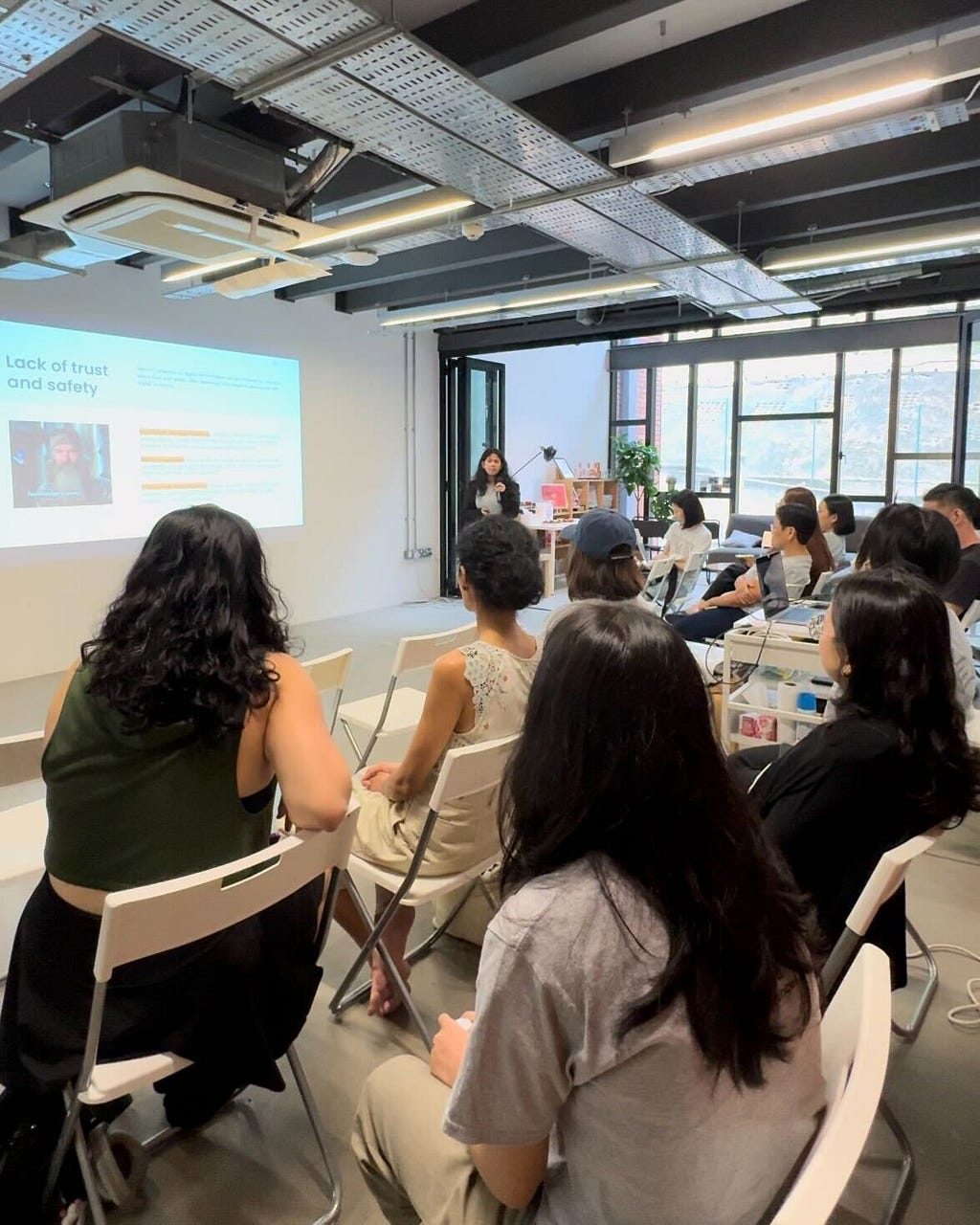 A woman is in front of an audience of seated people, presenting a powerpoint presentation on designing delightful digital experiences for the elderly