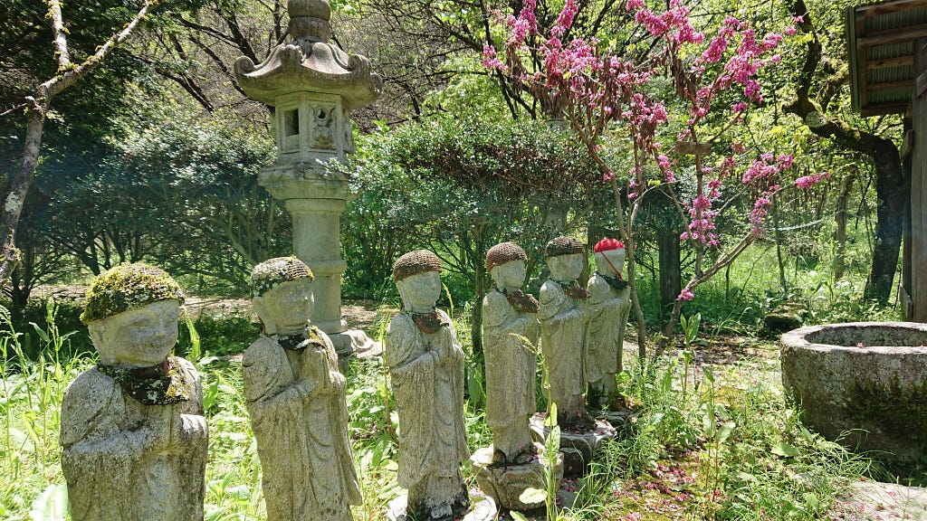 A row of stone statues at a shrine, wearing knitted hats