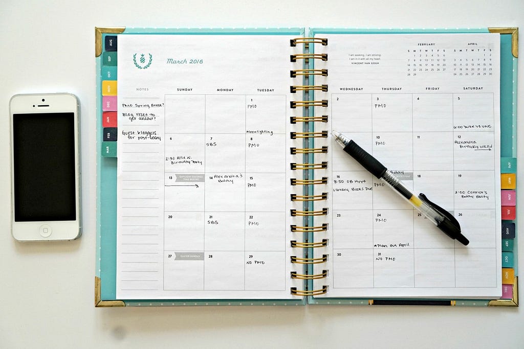 Image of a weekly planner together with a pen and a phone