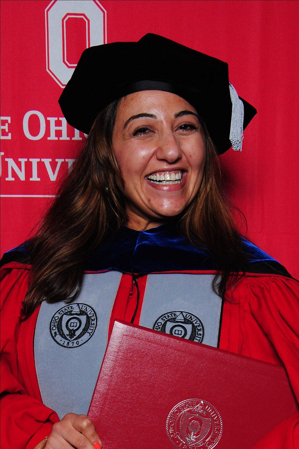 Mira Assaf Kafantaris in academic regalia, holding her PhD Diploma and grinning widely.