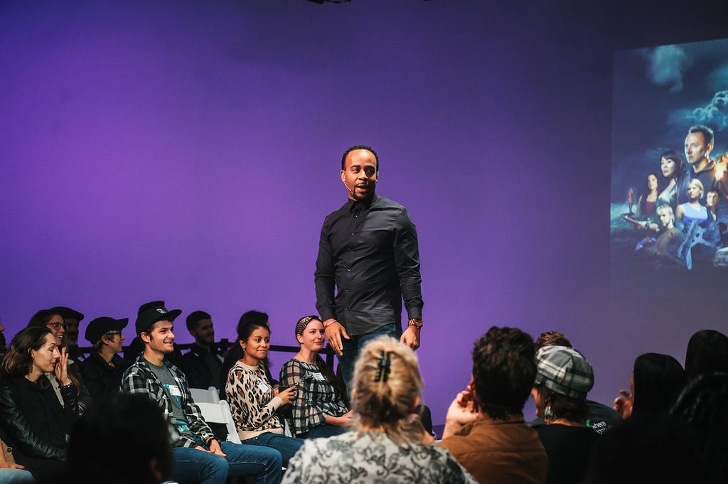 Our speaker Rashad Rayford presenting in a group of people. He is in the center of the image with a screen behind him.