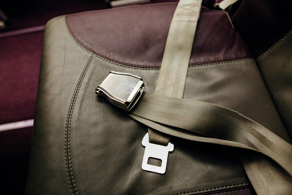 Unbuckled seatbelt on brown and maroon airplane seat