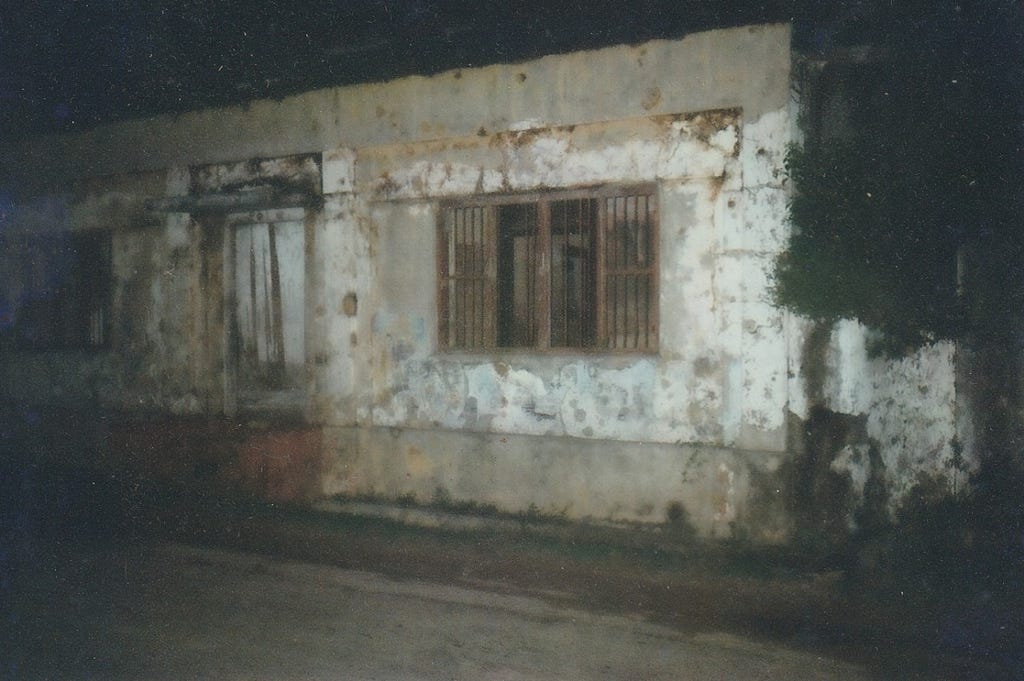 an old photograph of a burned building where only the walls and metal security bars of the windows remain.