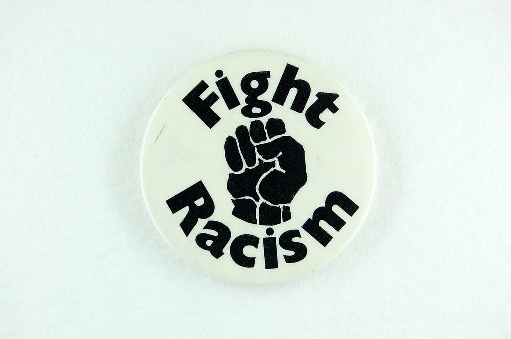 A pin badge showing a fist and the words ‘Fight Racism’ in black on a white background.