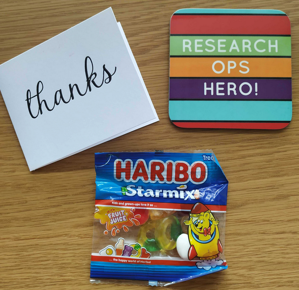 A packet of Haribo Starmix sweets, a small card with the word ‘thanks’ written on it, and a striped coaster displaying the words ‘ResearchOps hero’ are laid on a table.