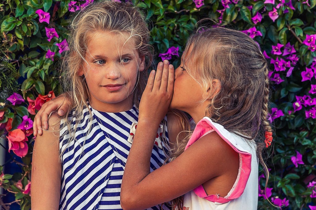 Two girls, one whispering to the other — a potentially judgmental secret
