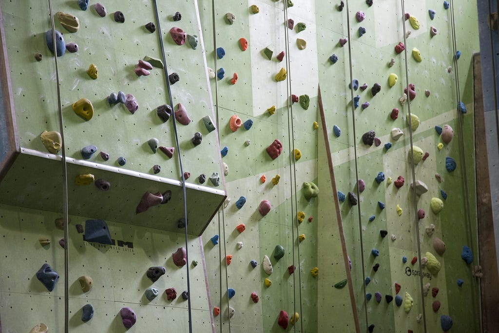 A picture of a large rock climbing wall with climbing ropes hanging from above.