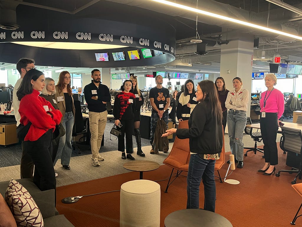 A group of young adults stand in a circle as they listen to a speaker in the CNN offices.