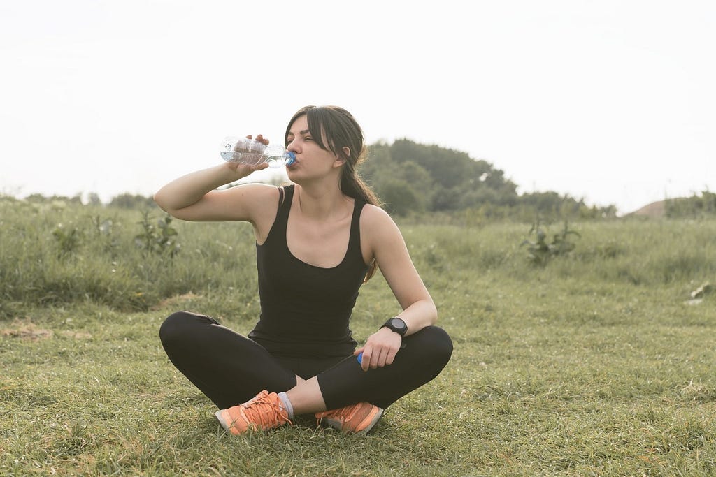 Woman sitting in a grassy field drinking a bottle of water