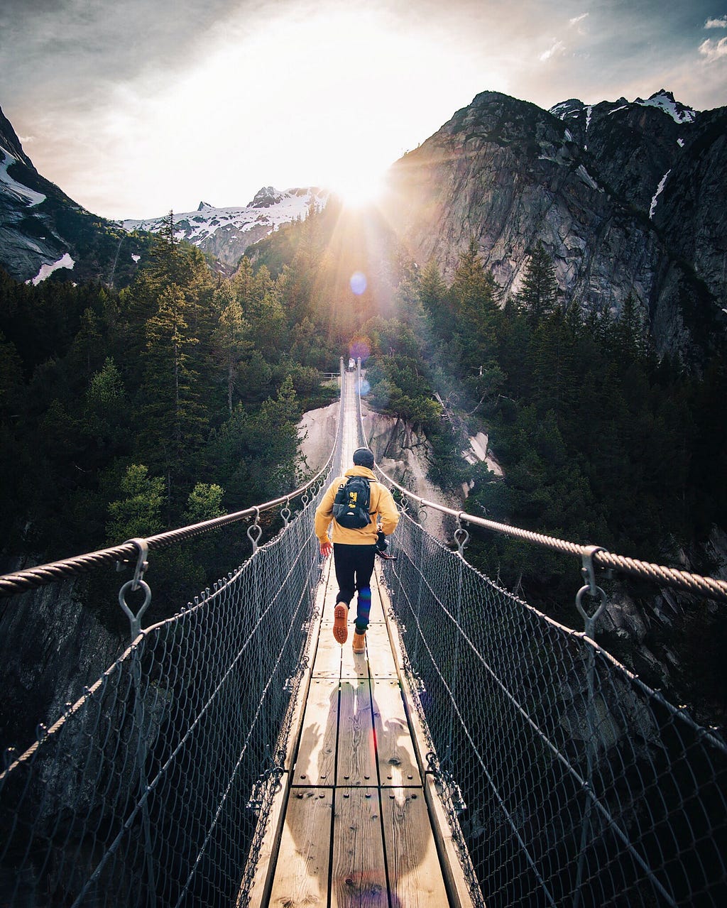 Man is running down a long, suspended bride high above the ground in some Swiss mountains.