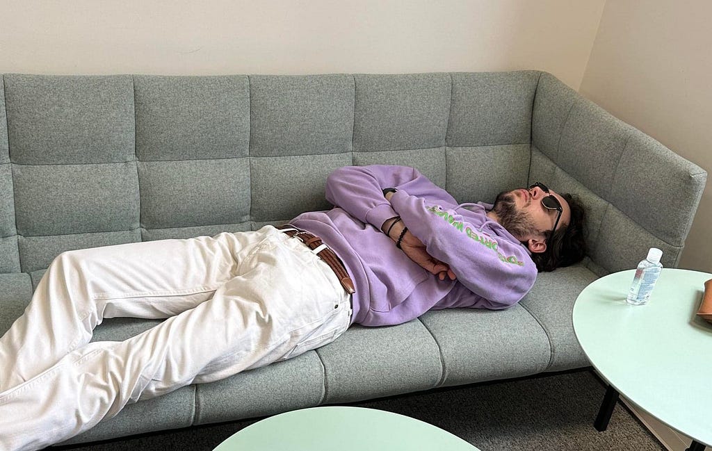 A beautiful male student sleeping on a couch while wearing a pair of sunglasses