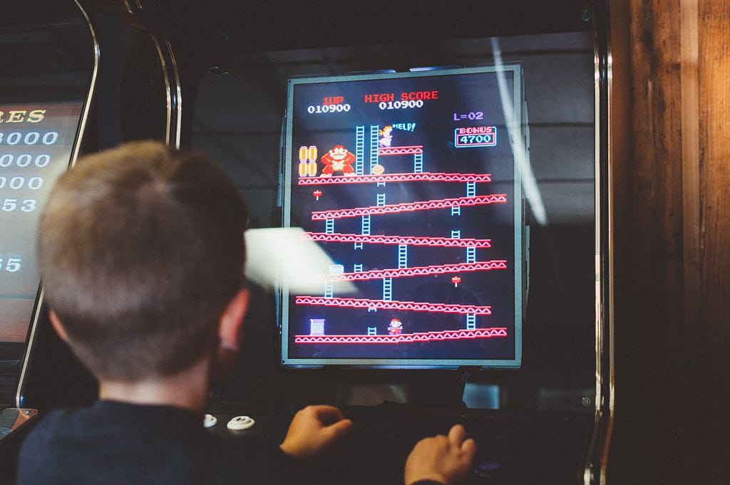Menino jogando um fliperama antigo do jogo Donkey Kong.