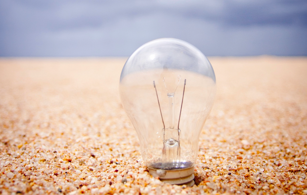 Light bulb in sand with blue sky horizon in the distance.