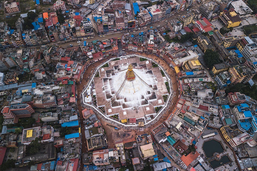 Bird’s-eye view of Boudhanath Stupa surrounded by Kathmandu, Nepal’s dense, colorful urban landscape.