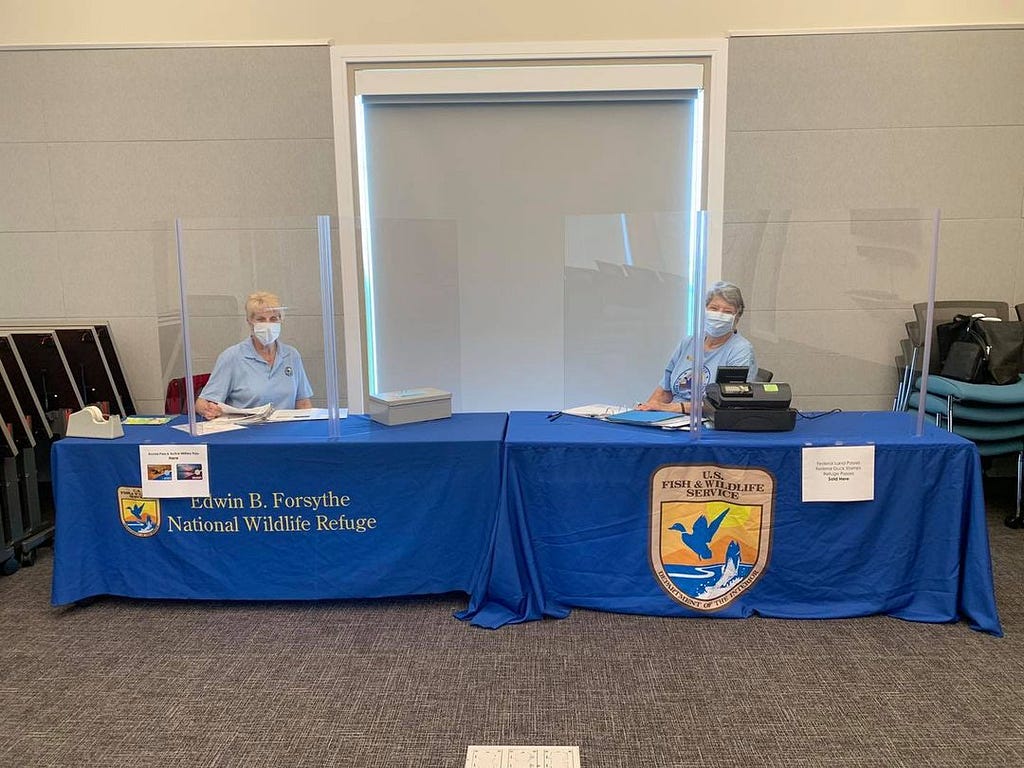Two uniformed staff members sit behind plexiglass at desks with the U.S. Fish and Wildlife Seal.