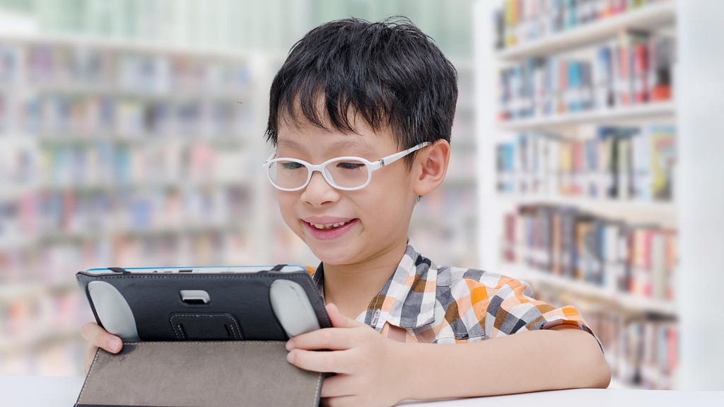 A photo of a boy sitting in a library practicing his oral reading fluency with a voice-enabled reading app.