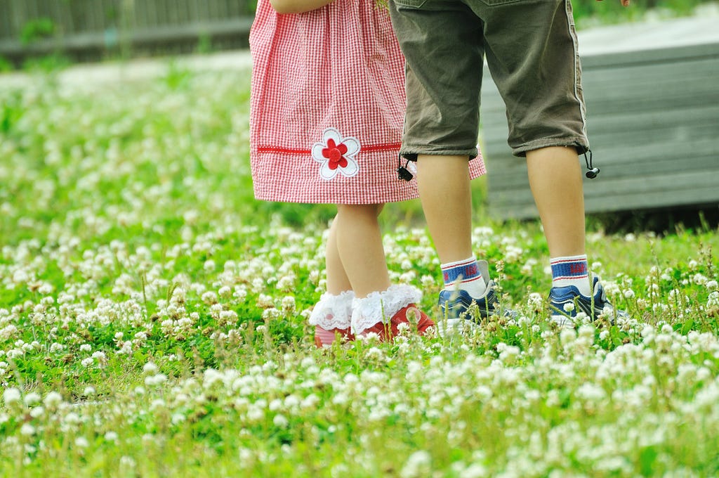 Two small children standing in the grass with their shoes on