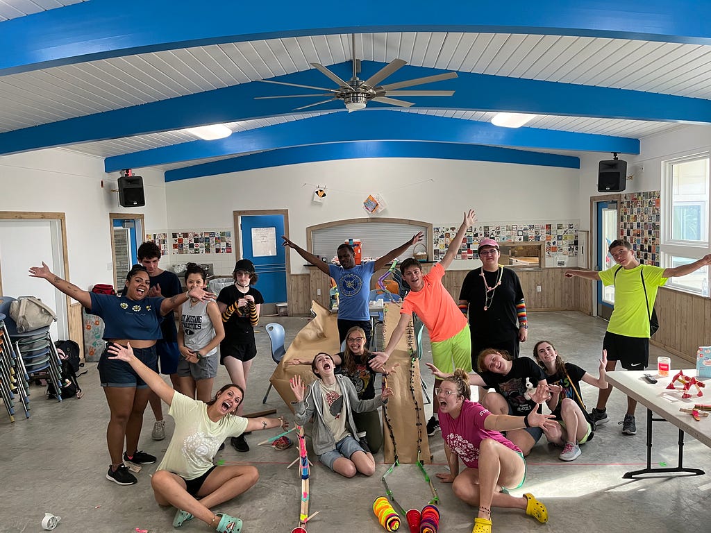 campers and staff gather arounnd their construction of a marbel tunnel and hold their arms out wide while they look excited for the camera