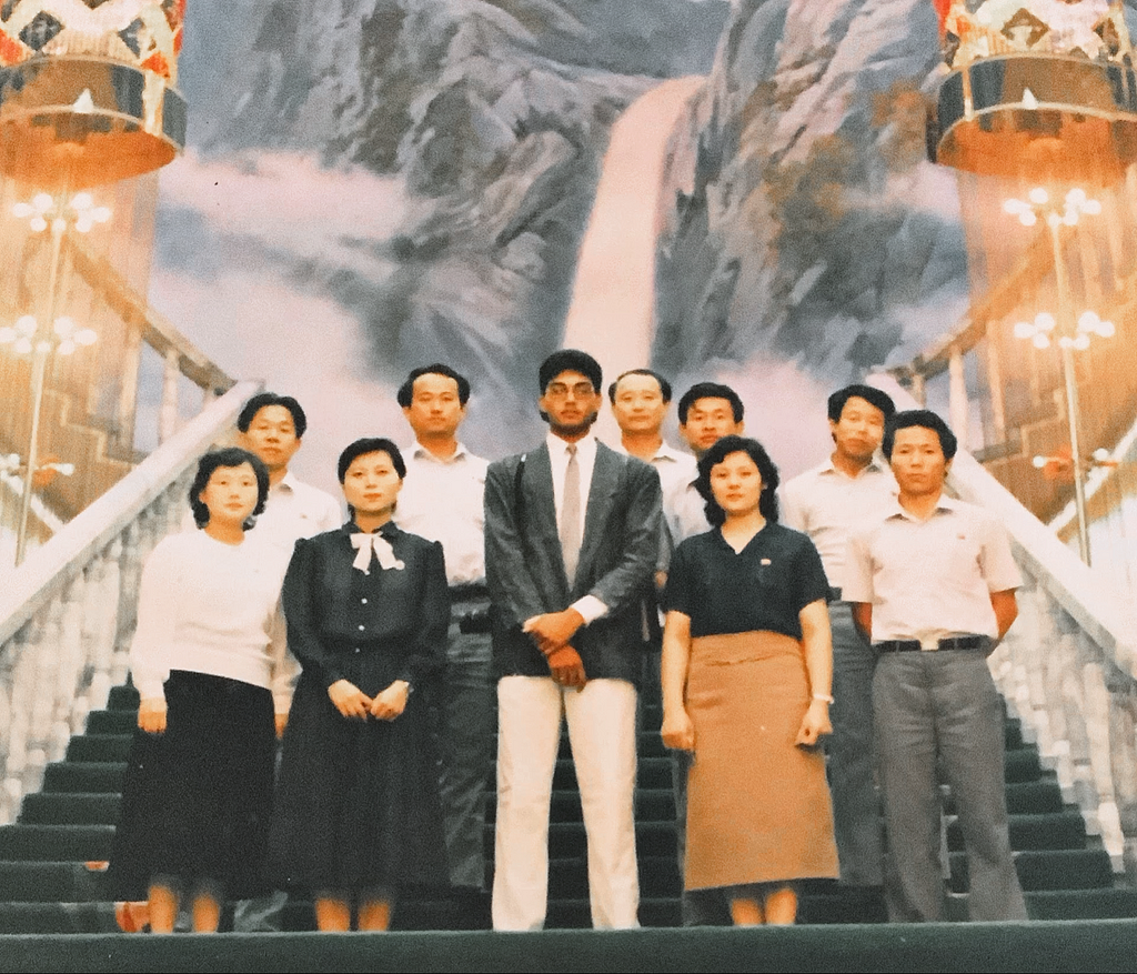 The picture depicts the author, standing mid nine North Korean, workers well, dressed in business casual attire. The author stands in the middle with a suit and tie. Behind them, as they stand on a staircase, is a painting of a waterfall coming down the side of a mountain.