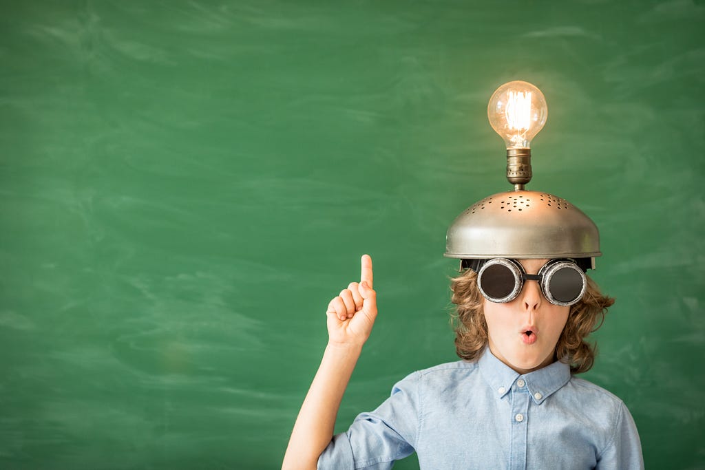 Child wearing a hat with a lightbulb on it holding finger up like he has an idea