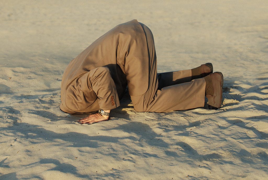 Om îmbrăcat în costum, cu capul înfipt în nisip.