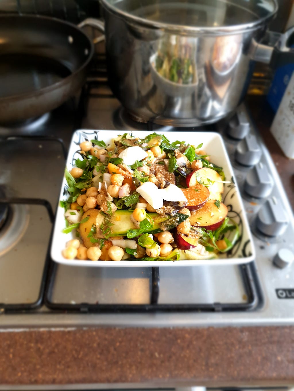 A gas hob with a bowl of food on it and two pans in the background.