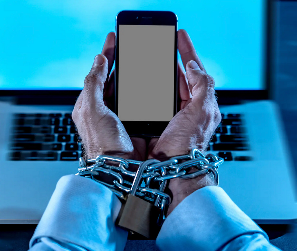 Photograph of man’s hands chained around a smartphone.