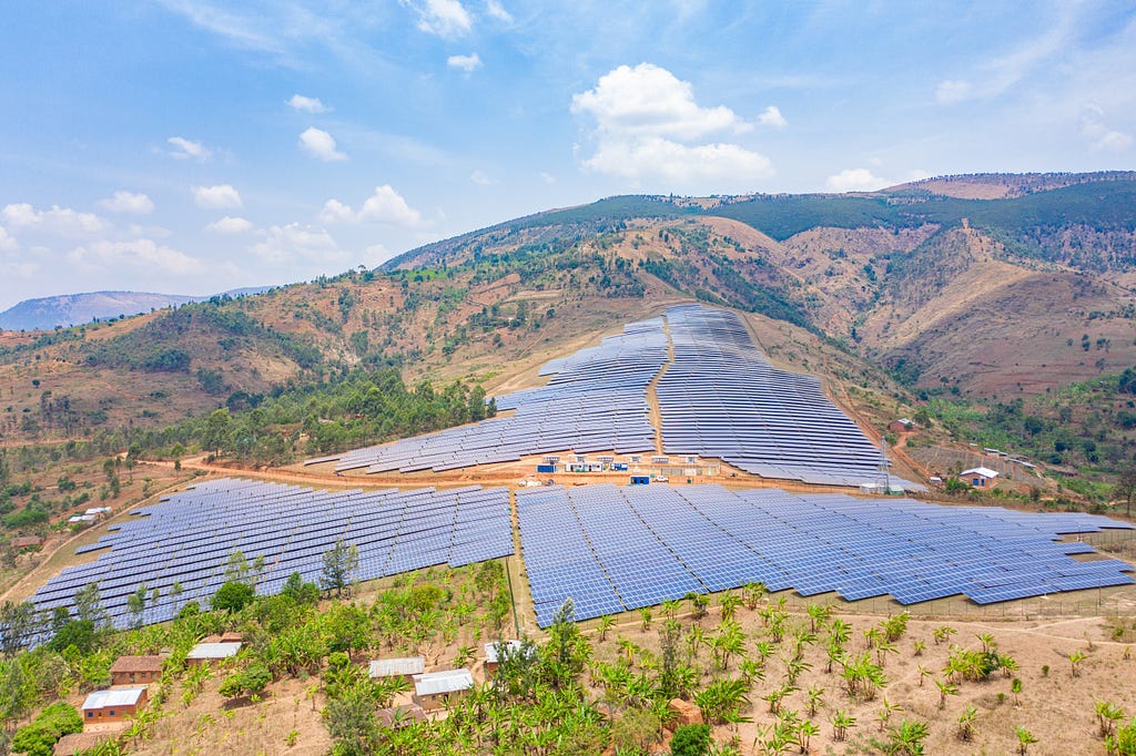 A large solar panel farm extends over a hilly landscape with green vegetation in Mubuga, Burundi harnessing renewable energy from the sun.