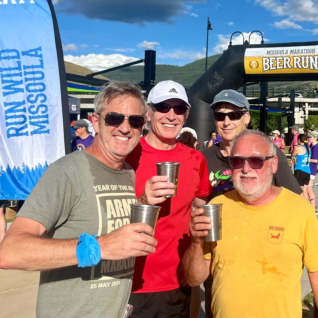 Four middle-aged runners in sunglasses holding beer glasses