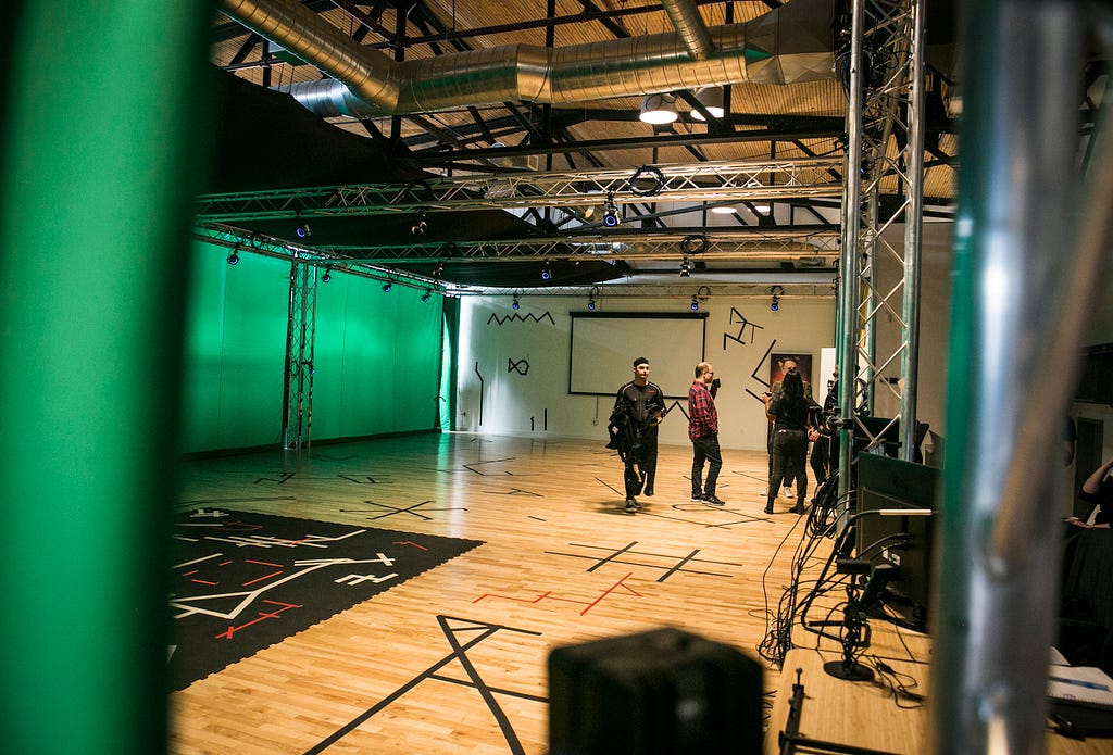 Five people stand in a motion-tracking room with a wall of green screens.