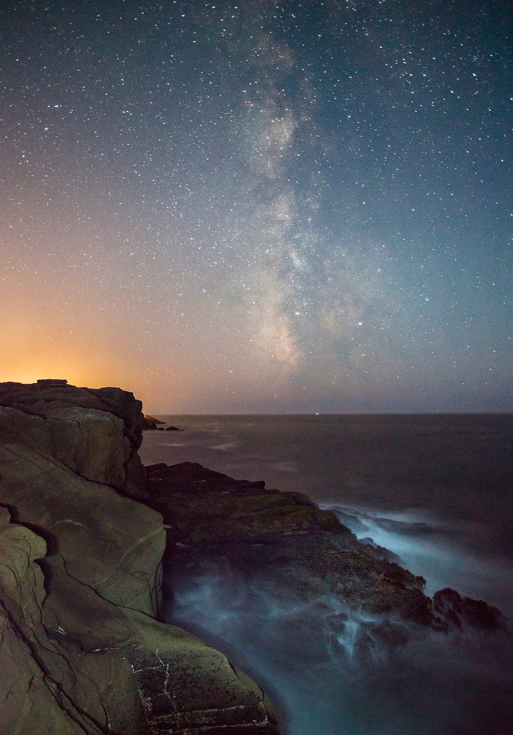 A night image of the Milky Way over the ocean and cliffs.