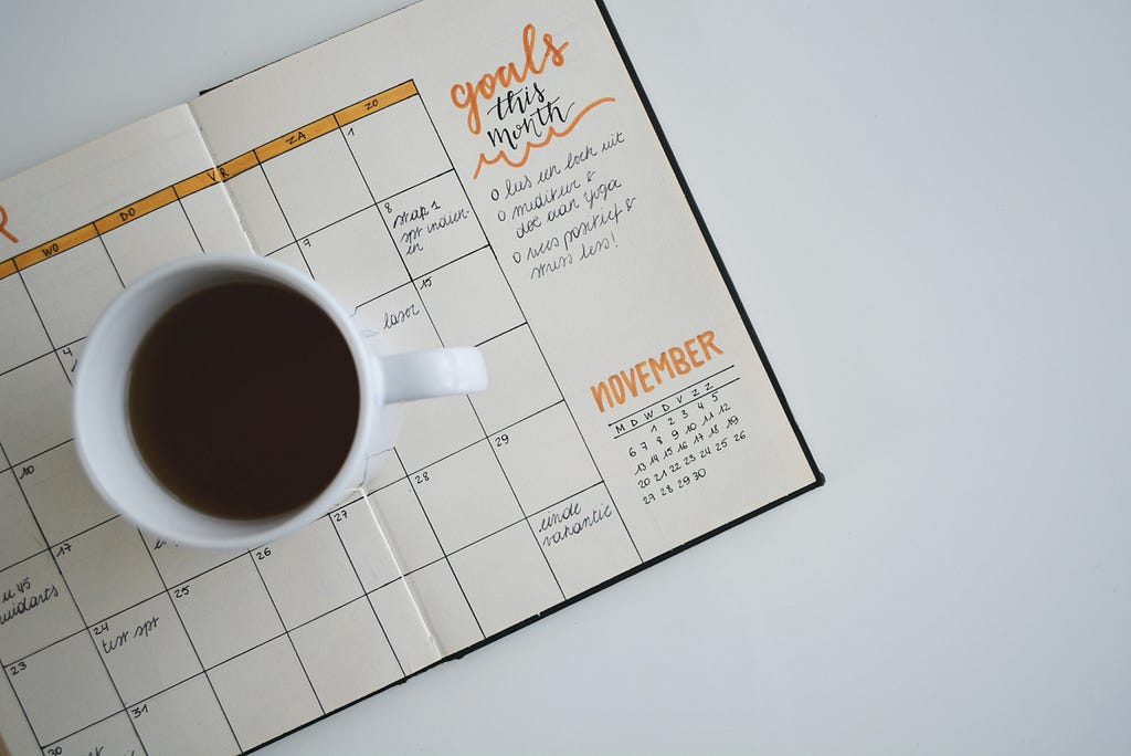 A coffe mug on a planner journal with goals written.