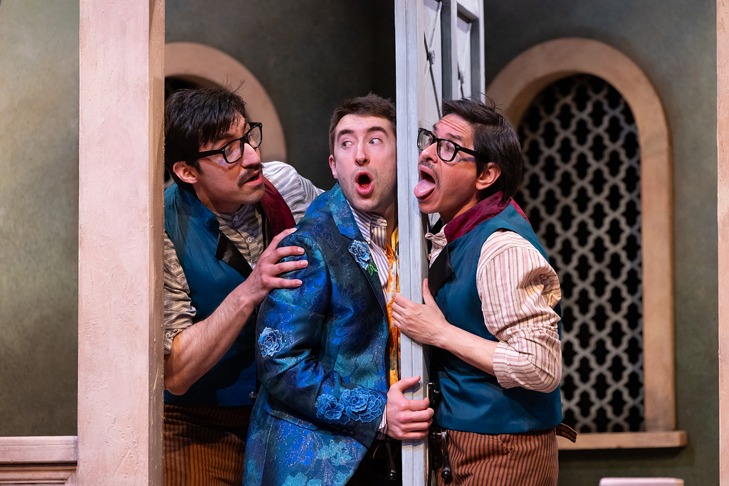 Two men stand on one side of a freestanding door while another stands on the other side. All three look overwhelmed with anger or excitement.