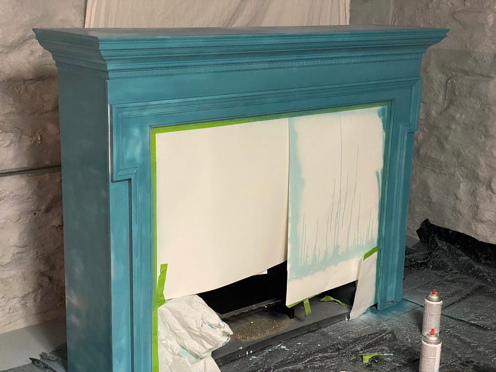 A fireplace mantle in the process of being spray-painted blue.