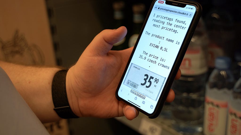 A hand holidng a mobile phone showing a screen with text extracted from a pricetag and a picture of the pricetag below the text.