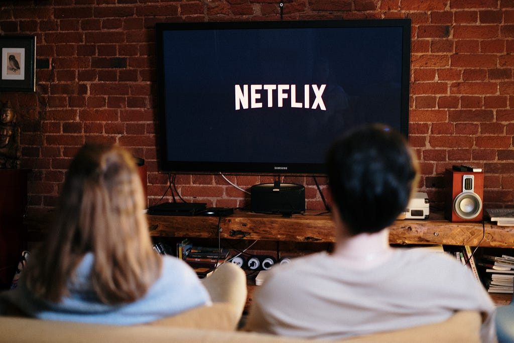 Man and woman sitting on a couch ni front of a television with Netflix