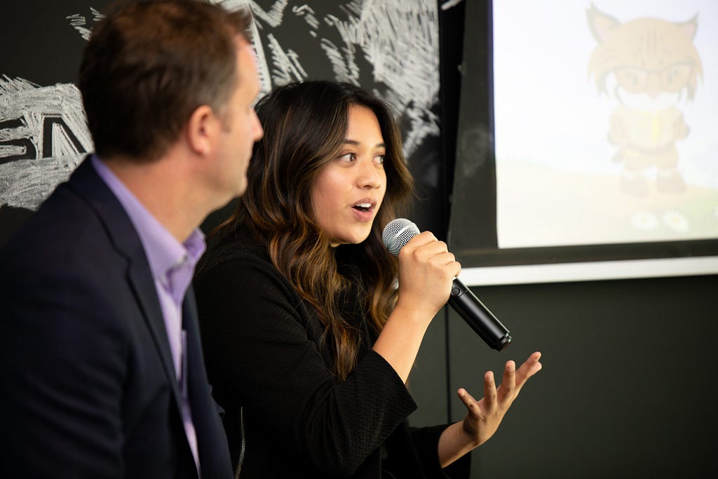 A woman with long, dark hair uses a microphone to speak at a Salesforce Partner event.