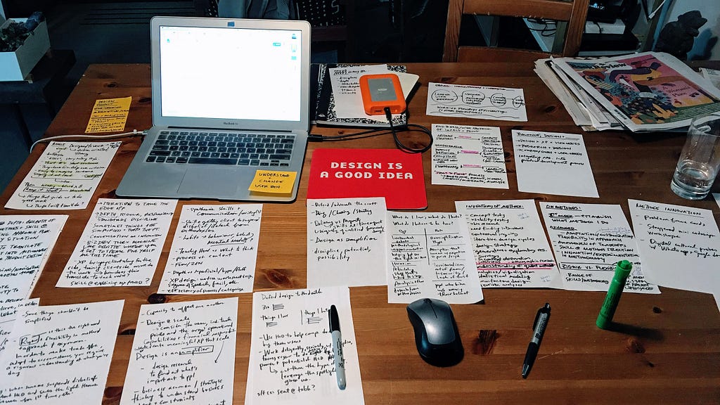 An open laptop sits on a wooden table covered with half sheets of handwritten notes