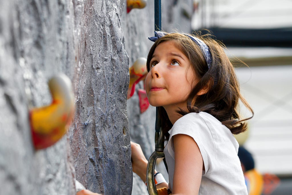 Young girl climbing a rock wall looking up a bit worried